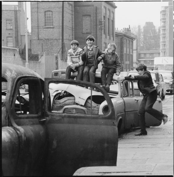 Four boys play on wrecked cars parked in the street: 1967