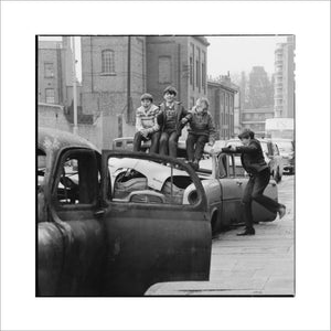 Four boys play on wrecked cars parked in the street: 1967