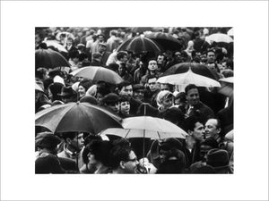 A crowd huddled underneath umbrellas in the rain: 1961